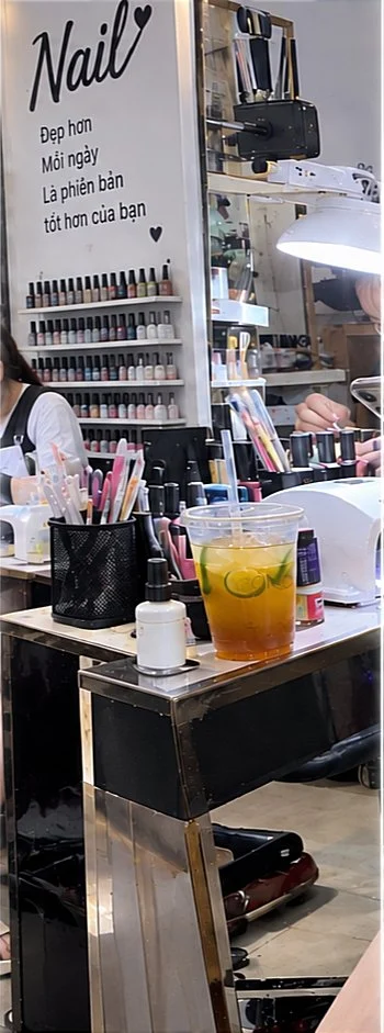 A narrow view into a salon shows a workstation surrounded by nail-polish displays, manicure supplies and drinks.